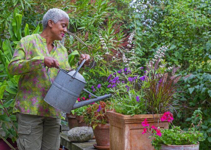 Arit Andersen geeft een pot vol zomerse planten, zoals verbena en pennisetum, water.