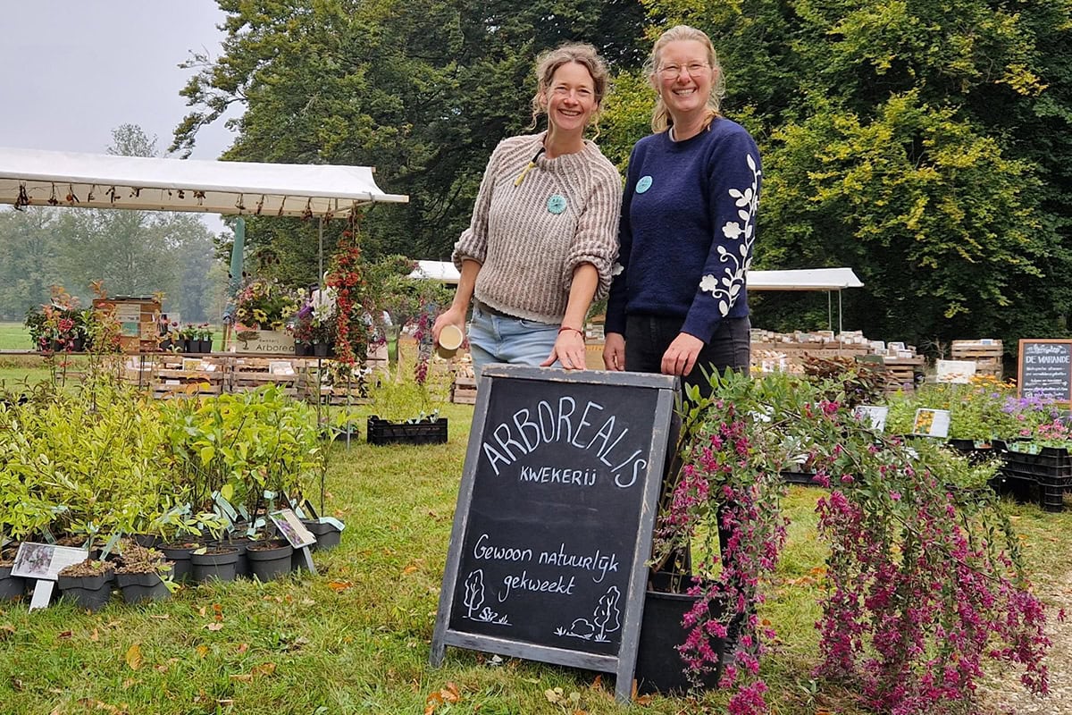 Twee vrouwen bij een bord tussen de planten, waaronder Lezpedeza