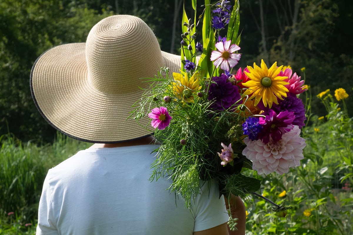Vrouw met hoed draagt bos bloemen over haar schouder.