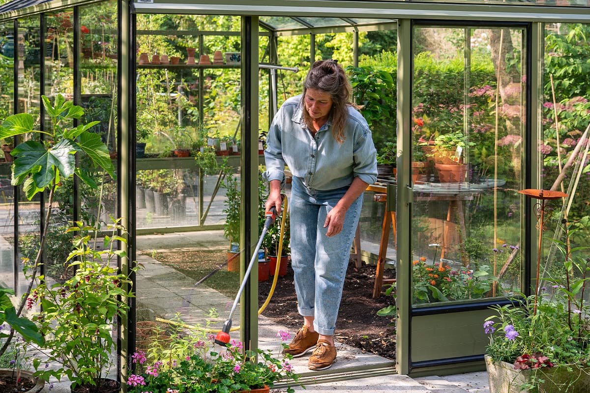 Martine geeft planten water in de kas.