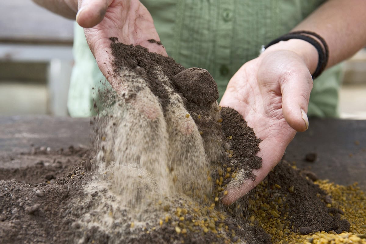 Iemand mengt zand met compost, met de hand.