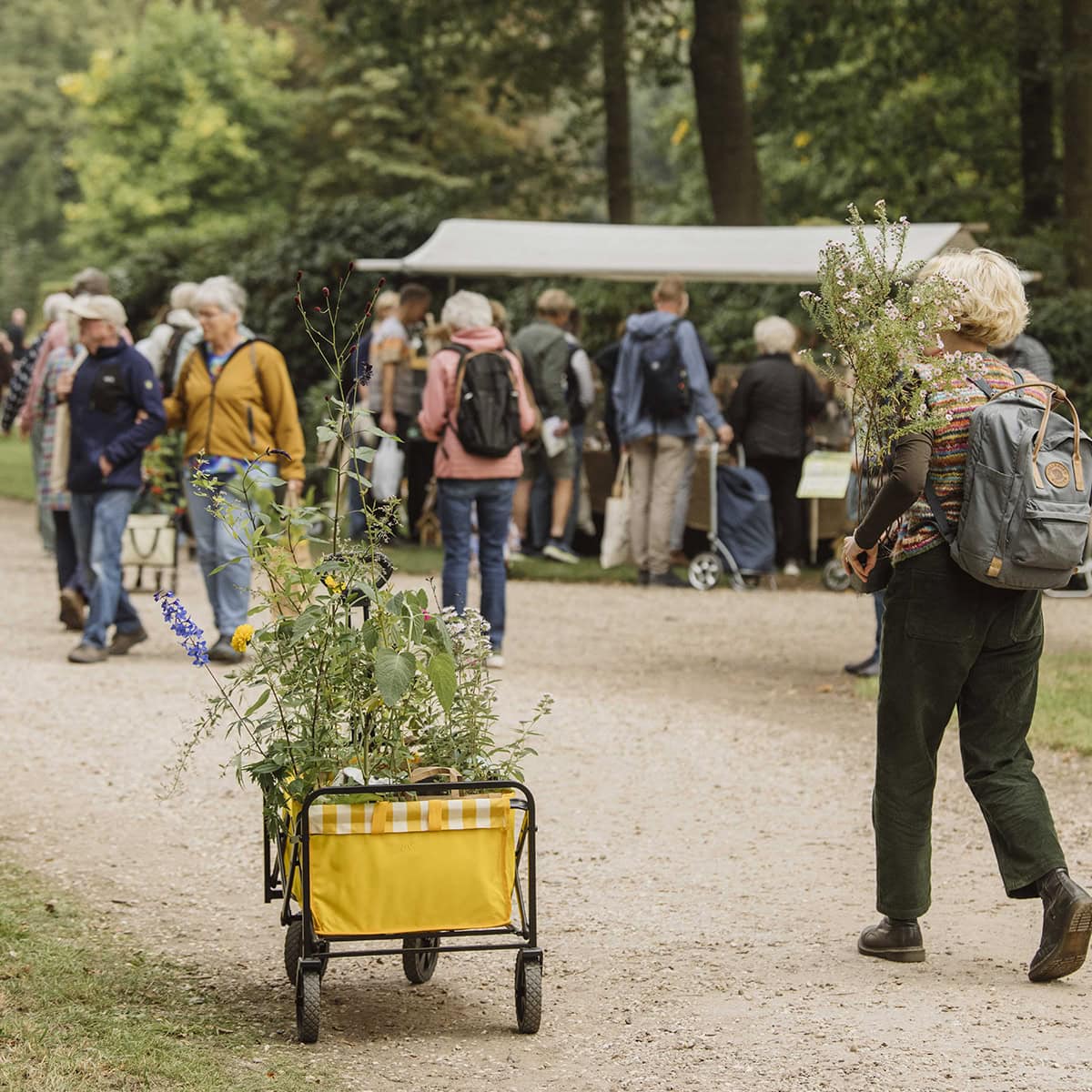 Kar met planten en vrouw die planten draagt.
