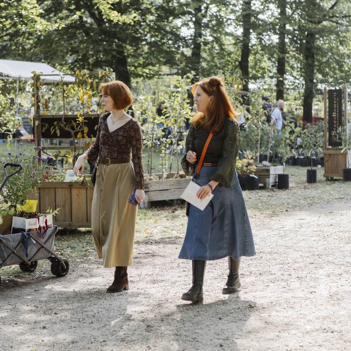 Twee vrouwen wandelen langs kramen met planten.
