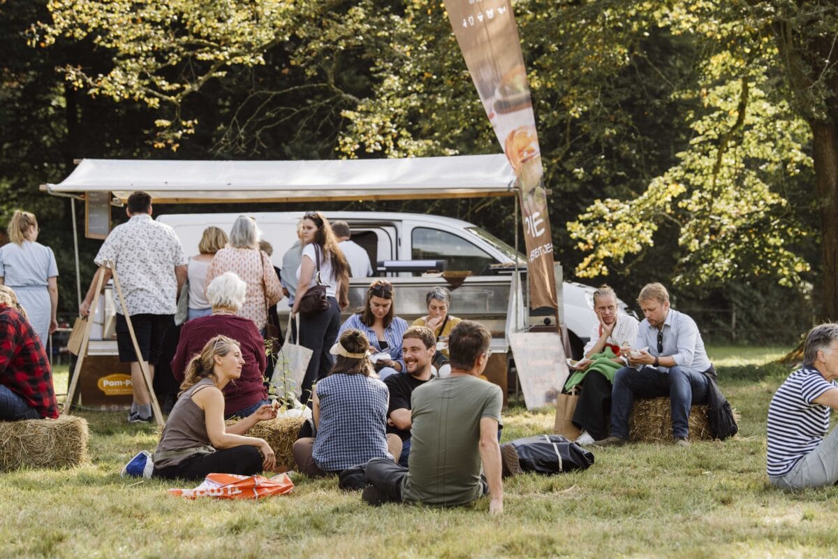 Mensen zitten bij de foodtrucks op strobalen en op de grond.