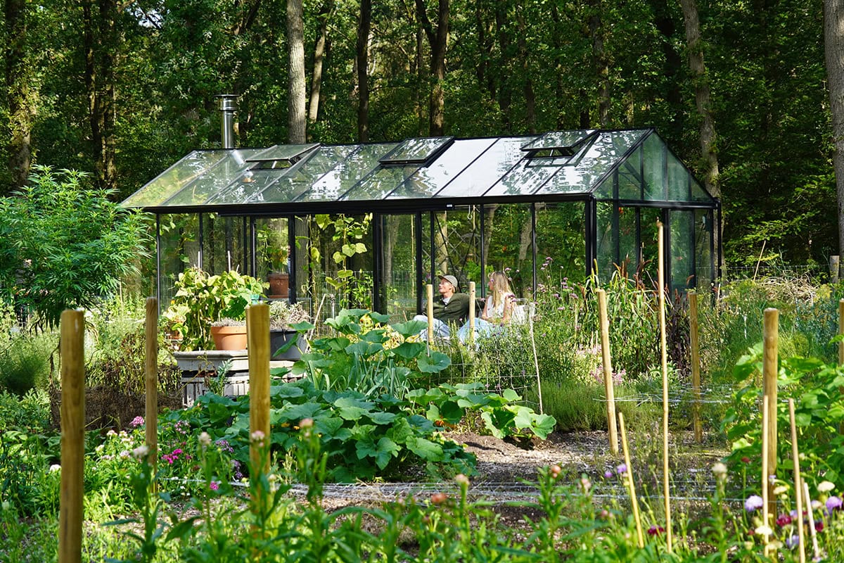 Kas in groene tuin met twee mensen op een bankje
