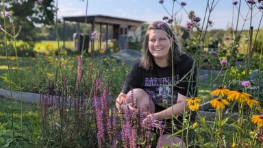 Hester zit geknield bij bloeiende planten in haar nieuwe border.