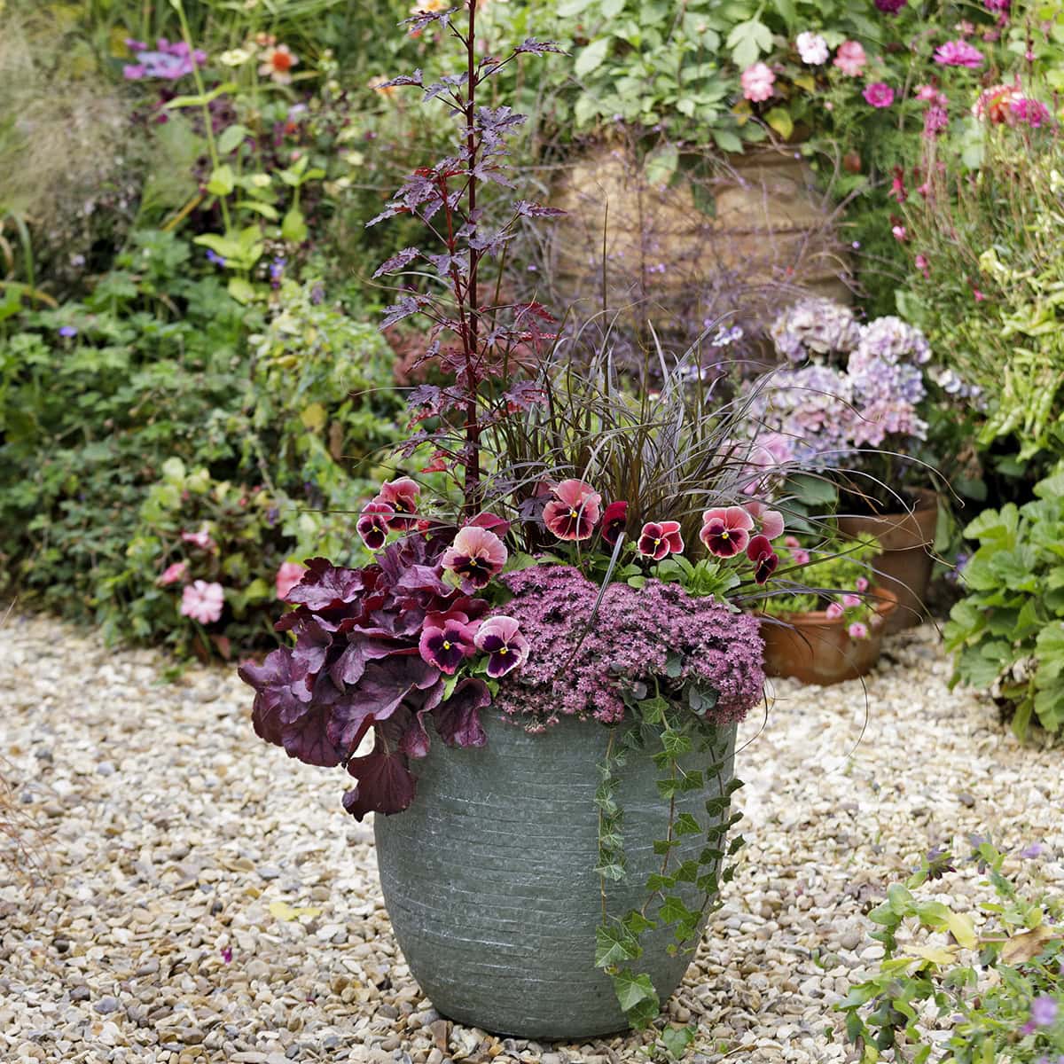 Een buitenpot met verschillende roze bloemen en bladeren.