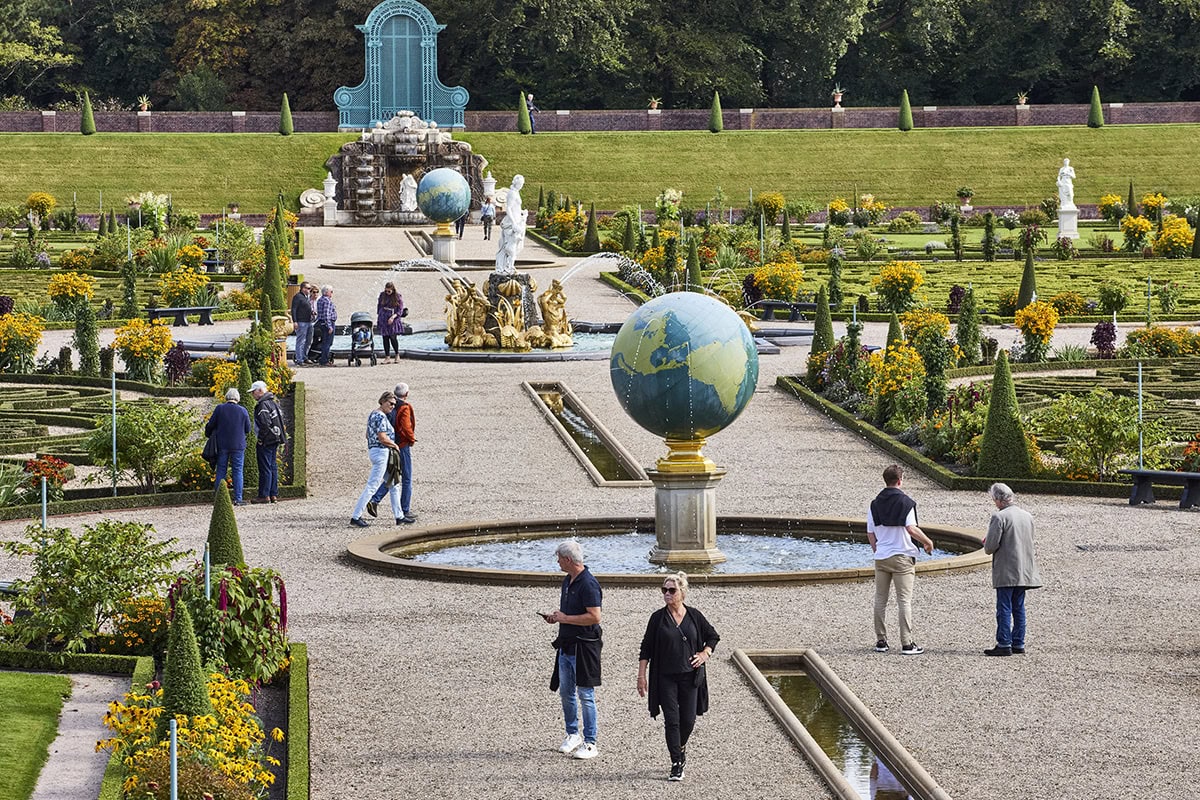 Mensen wandelen in de tuinen van Paleis Het Loo: groen en kunstornamenten.