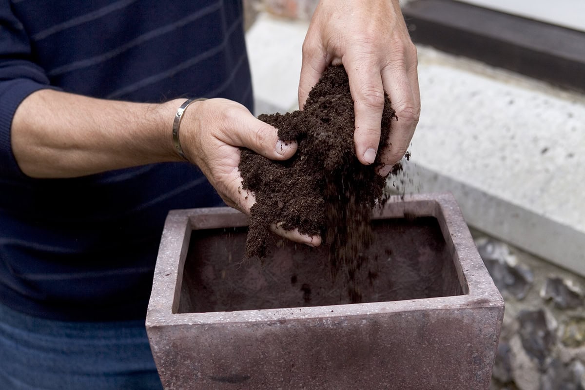 Iemand stopt aarde in een buitenpot, om te gaan beplanten.